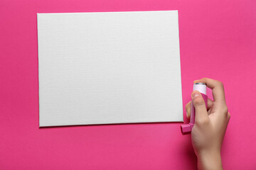Child's hand with asthma inhaler and blank card on pink background