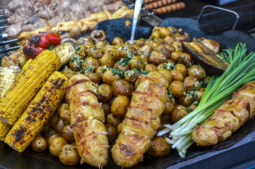 Vibrant display of grilled vegetables including golden corn, seasoned potatoes, and fresh herbs,...