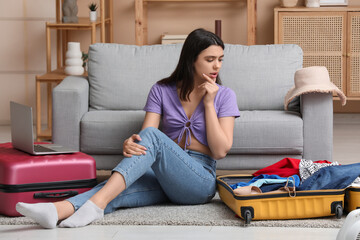 Thoughtful young woman with suitcases near sofa in living room