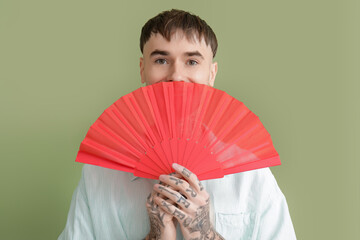 Young tattooed man with hand fan on green background, closeup