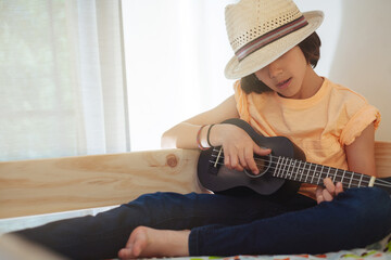 Boy playing ukulele with straw hat during a quiet moment on bed