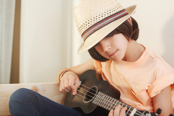Boy playing ukulele with straw hat in soft morning light