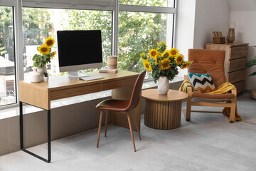 Beautiful workplace with computer and sunflowers in interior of cozy room