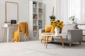 Interior of living room with sofa, workplace and sunflowers on coffee table