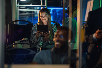 Young woman using tablet while riding bus at night