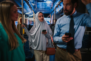Muslim woman wearing hijab using smartphone on bus with businessman and passenger