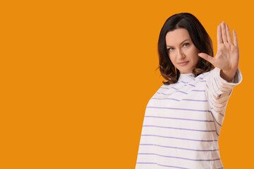 Beautiful displeased mature woman showing stop gesture on yellow background