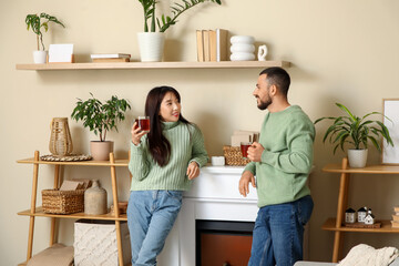 Loving young happy couple with cups of hot tea near fireplace at home