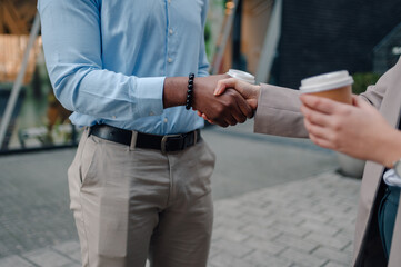 Business people shaking hands outdoors holding takeaway coffee