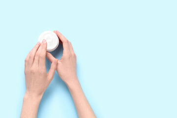 Beautiful female hands with jar of cosmetic cream on blue background