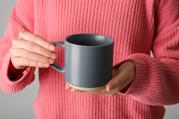 Woman in stylish sweater with ceramic mug against grey background, closeup