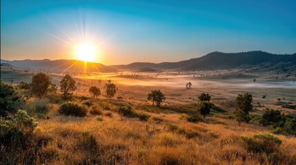 Fototapeta premium Sunrise over distant hills casting golden light on floating morning fog
