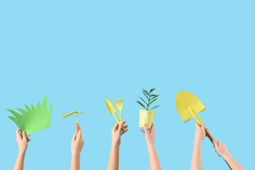 Female hands with gardening tools, plant and paper grass on blue background