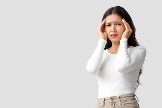 Young Asian woman suffering from headache on grey background. Brain Injury Awareness Month