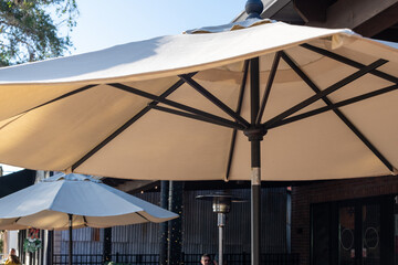 Multiple tan-colored fabric sunshades opened on a patio with black metal poles and hand cranks. The parasol has vents at the top of the poles. There are propane patio heaters among the beige shades.