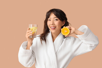 Young Asian woman with citrus infused water on beige background