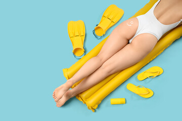 Lying woman with inflatable mattress and beach accessories on blue background