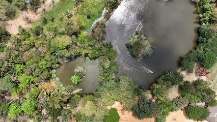 Breathtaking aerial drone shot of the Achimota Forest (Ghana), reveals a winding, dark water body snaking through a dense, vibrant jungle or rainforest, with a small boat creating ripples.