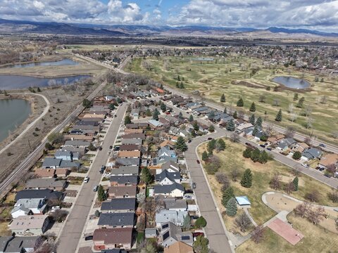 Showcasing a quiet suburban neighborhood in the Denver Front Range, featuring rows of single-family homes adjacent to a large golf course with lakes and open green spaces.