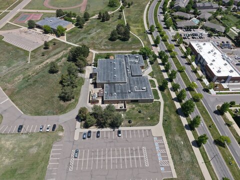 Aerial drone view of a school campus in Lowry, Colorado, featuring large buildings, extensive parking, and adjacent recreational facilities like a running track and tennis courts.
