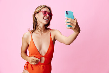 Vibrant summer vibes young woman in orange swimsuit snaps a selfie against a bright pink backdrop
