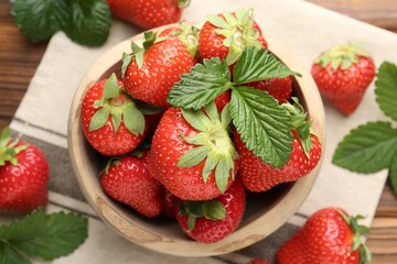 Fresh ripe strawberries and leaves in bowl on wooden table, flat lay