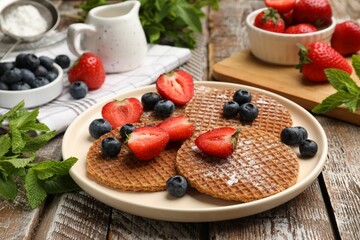 Tasty Dutch waffles (stroopwafels), mint and berries on wooden table, closeup