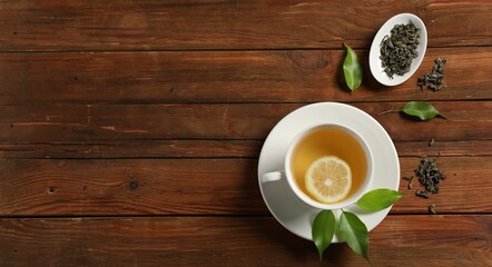 Tasty green tea with lemon in cup, brew and leaves on wooden table, flat lay. Space for text