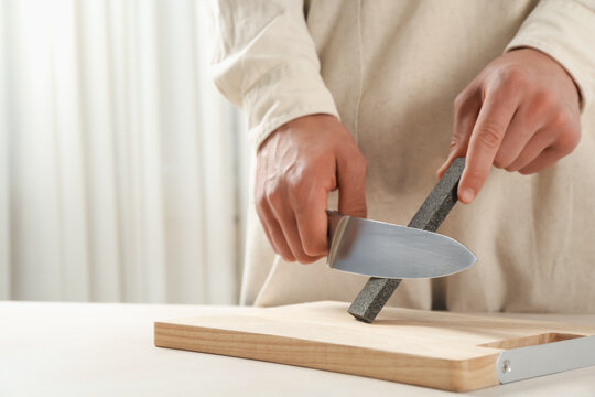 Man sharpening knife with sharpener at beige table indoors, closeup. Space for text - Powered by Adobe