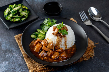 Chicken in brown sauce or gravy sauce with rice  on a black plate - Asian food style