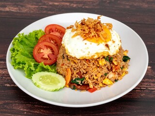 Classic Indonesian Nasi Goreng, a popular stir-fried rice dish, served with a crispy fried egg, crackers, and fresh vegetables on a wooden table.