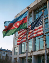 two flags, one of Azerbaijan and one of the United States, flutter in the wind outside a dilapidated building