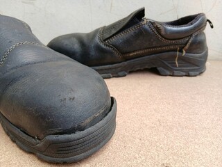 Old black safety shoes were broken on the wooden board. 