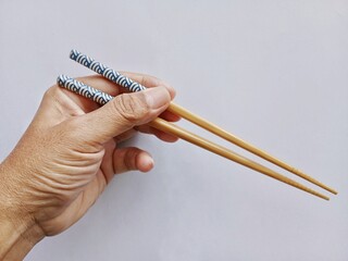 Close up of hands holding bamboo chopsticks in front of a light background.