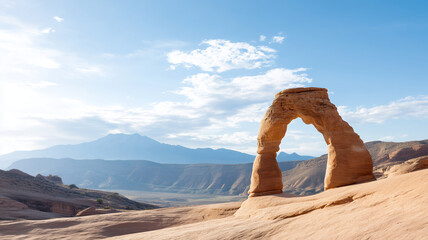 Natural sandstone arch formation stands against blue sky with clouds and distant mountain range in desert landscape