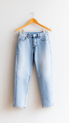 Light blue denim jeans hanging on wooden hanger against white wall, casual fashion style, relaxed and minimalistic vibe