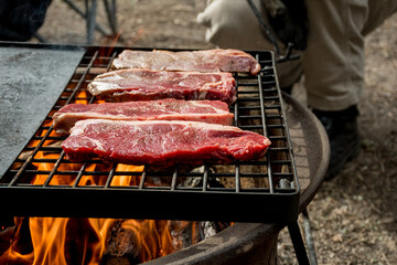 Beef steaks grilling on a cast iron grlill plate on a camp fire. Campfire cooking. Outdoor BBQ