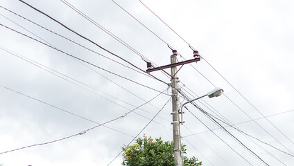 Utility pole ascends into a hazy sky, carrying a network of wires and a streetlight fixture.