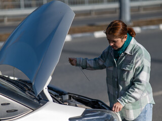 Caucasian female driver checking oil level in car engine.