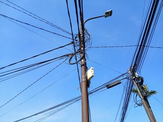 Bottom angle view of messy power cables on poles with blue sky background.