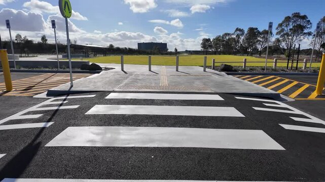 Modern pedestrian crossing with tactile paving and bollards for accessibility, near a public park in Australia. Crosswalk features safety markings and accessible design in Australia.