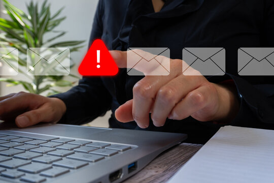 A businesswoman in front of a computer pointing at a virtual warning sign, alongside many email icons. Spam or phishing concept.