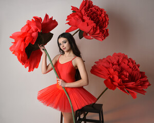 Close-up portrait of ballerina holding oversized red flower in golden light, brunette model in red...