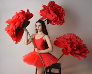 Close-up portrait of ballerina holding oversized red flower in golden light, brunette model in red...