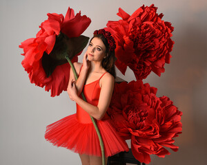 Close-up portrait of ballerina holding oversized red flower in golden light, brunette model in red...