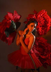 Close-up portrait of ballerina holding oversized red flower in golden light, brunette model in red...