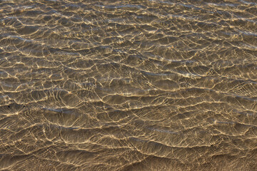 Mesmerising natural liquid patterns of crystal clear ocean water glistening in the shallows of an idyllic clean shoreline. 