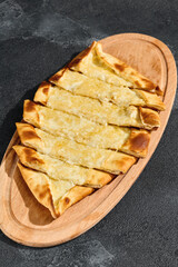 Cheese pide with golden crust, bright lighting, overhead composition on wooden serving board
