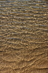 Mesmerising natural liquid patterns of crystal clear ocean water glistening in the shallows of an idyllic clean shoreline. 