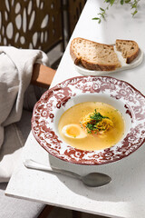 Chicken broth with egg and noodles, bright natural lighting, overhead composition